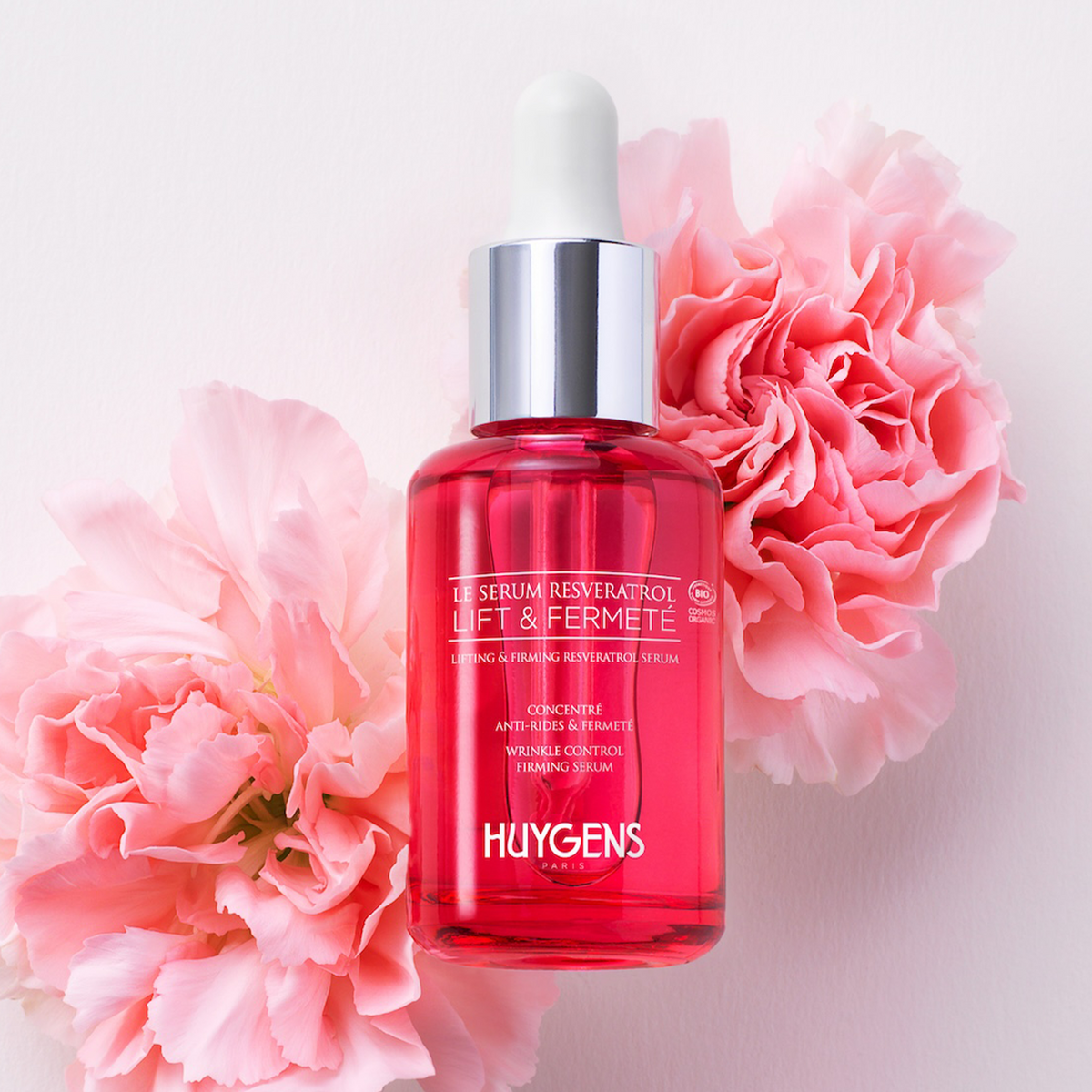 Flacon du sérum posé parmi des œillets roses